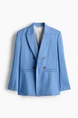 Blazer cruzado celeste de manga larga con solapas de pico, hombreras y bolsillos frontales con solapa. Presenta cierre de doble botonadura con botones oscuros y forro interior.