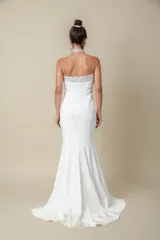 Vestido largo blanco de crepé, corte sirena, palabra de honor con bordado de piedras en el escote y cola pequeña.