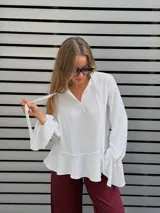 Blusa blanca de textura arrugada, con escote en V y lazos para anudar. Presenta mangas largas con puños acampanados y un diseño con volado en el ruedo.