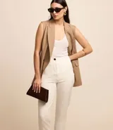 Pantalón de sastrería estilo carrot color blanco, de tiro alto, con trabillas en la cintura y cierre frontal de cremallera y botón.