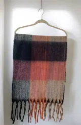 Bufanda de gran tamaño con diseño de cuadros en tonos naranja, rosa, gris, negro y beige, con flecos en los extremos.