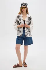 Camisa de viscosa de corte holgado, color blanco con estampado negro de paisaje con palmeras, cuello camisero y cierre frontal con botones.