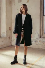 Tapado de lana color beige, de corte recto y largo medio, con solapas clásicas, cierre frontal de botones y bolsillos laterales amplios.