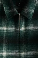 Sobrecamisa de lana con acabado cepillado, diseño a cuadros en tonos verde oscuro, negro y blanco. Cuenta con cuello inglés, cierre bidireccional frontal y bolsillos laterales discretos. Forrada y de corte regular.