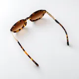 Lentes de sol con armazón ovalado estilo carey (tortoise) en tonos marrones y negros, con detalles metálicos dorados en las patillas y lentes degradados en tono marrón.