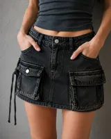 Mini falda tipo cargo de denim negro con efecto lavado, tiro bajo, bolsillos frontales tipo cargo con solapa y detalle de tiras laterales colgantes.