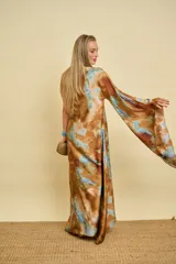 Vestido túnica largo de satén con diseño de un solo hombro, una manga larga amplia y estampa tipo tie-dye en tonos marrón y celeste.