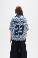 Remera tipo chomba de manga corta con cuello camisero, confeccionada en tejido con estampado de tablero ondulado en tonos rosado y blanco, con franja horizontal y detalles gráficos en color bordó.