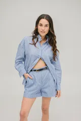Conjunto de dos piezas compuesto por una camisa de corte oversize con cuello camisero y mangas largas, y un short de tiro alto con dobladillo en el ruedo. Ambas prendas presentan un diseño a rayas verticales en tonos azul y blanco e incluyen un cinturón fino de cuero negro.