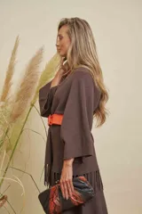 Saco largo color chocolate con cuello en V, mangas anchas y detalle de flecos en el ruedo. Se ajusta con un cinturón ancho color naranja.