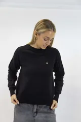 Buzo de tejido fino negro con delicados destellos brillantes integrados en la trama. Presenta cuello redondo, mangas largas con corte ranglán y terminaciones acanaladas en cuello, puños y cintura.