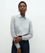 Suéter de punto gris con cuello redondo y diseño de cuello camisero celeste superpuesto. Presenta mangas largas y terminaciones acanaladas en puños y cintura.