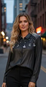 Camisa de manga larga en color gris oscuro con acabado brillante. Presenta un cuello clásico con apliques de pedrería, detalles bordados con líneas curvas y perlas decorativas en el frente, y paneles texturizados en los hombros.