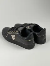 Zapatillas deportivas de cuero sintético en color blanco, beige y negro, con cordones y aplique decorativo dorado con forma de moño.