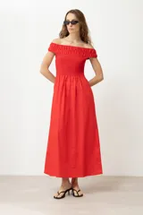 Vestido largo de color rojo con escote bardot y cuerpo elástico tipo nido de abeja. Presenta una falda de corte evasé con bolsillos laterales.