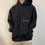 Canguro negro oversize con capucha y bolsillo tipo canguro. Presenta una estampa pequeña con la frase "feel the vibes" en el pecho y un logo en la parte inferior.