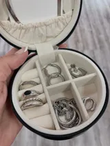 Alhajero circular negro con cierre de cremallera y forro interior de terciopelo beige. Cuenta con compartimentos para anillos y otros accesorios.