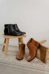 Botas cortas de cuero negro con paneles traseros de gamuza, cierre lateral y detalle de correa con hebilla metálica en el tobillo.
