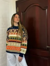 Sweater de lana merino con estampado Fair Isle en tonos azul marino, beige, naranja, verde oliva y bordó. Tiene cuello redondo y mangas largas.