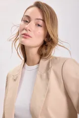 Blazer de color visón con mangas tres cuartos, solapas clásicas y cierre frontal con un botón. Presenta bolsillos laterales con solapa.