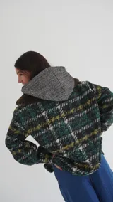Buzo canguro oversize de paño de lana gris con capucha estampada y cuello de corderito blanco. Cuenta con aberturas laterales en el ruedo y detalles de cuero sintético marrón en el cierre frontal y etiqueta.