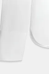 Camisa de cuello solapa y escote en pico, con manga larga y cierre frontal mediante botones. Presenta un diseño fluido con bajo asimétrico y aberturas laterales.