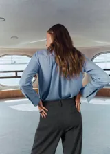 Pantalón de traje gris con sutil diseño de cuadros, tiro medio y pernera recta. Cuenta con trabillas para cinturón, pinzas delanteras, bolsillos laterales y cierre frontal con cremallera, botón y ganchos ocultos.
