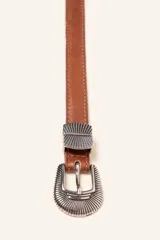 Cinto de cuero marrón de estética western, con costuras pespunteadas y herrajes metálicos plateados con diseño grabado en la hebilla y los pasacintos.