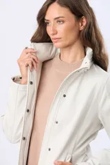 Campera de neopreno en color blanco hueso, con cierre frontal y botones a presión. Presenta cuello alto, mangas largas y bolsillos laterales. Diseño funcional y versátil para uso diario.