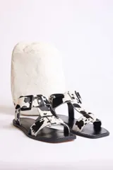 Sandalias planas con diseño de estampado animal print tipo vaca, con puntera cuadrada, tira en T y cierre con hebilla ajustable en el tobillo.
