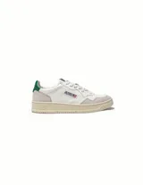 Championes de estilo vintage inspirados en los años 80, confeccionados en cuero blanco con paneles de gamuza gris en la puntera y el talón. Presentan perforaciones en la puntera para mayor ventilación, cordones planos de algodón y un detalle en color verde en el talón. La suela es de goma en tono crema con el logo de la marca.