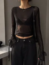 Top de manga larga confeccionado en tejido de tul transparente, con cuello redondo y detalle de lazos ajustables en los puños.