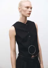 Chaleco de sastre color negro, con cuello en pico y cierre frontal de botones. Presenta un diseño recto, sin mangas y cuenta con dos bolsillos de ribete en la parte delantera.