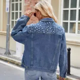 Campera de jean color negro con apliques de perlas en la parte superior frontal. Presenta cuello clásico, cierre frontal con botones metálicos y dos bolsillos en el pecho.