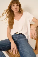 Remera blanca de poliéster y algodón, con escote en V, corte relajado, bordes sin rematar, detalles de costura central expuesta y dobladillo estilo camisero.