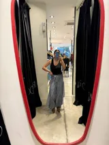Pantalón de corte amplio y fluido, color gris con acabado satinado, con cintura elástica y lazo ajustable. Presenta un diseño con paneles laterales que aportan volumen y movimiento.