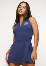 Vestido azul marino sin mangas, con cuello en V y falda corta con diseño cruzado. Presenta un logo bordado en el pecho. Incluye short interno y protección UV50+.