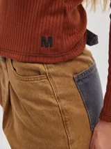 Camiseta negra de manga larga, con tejido acanalado, cuello redondo a la base y corte tipo crop. Presenta costuras rojas a la vista y un logo "M" bordado en rojo en el lateral izquierdo.