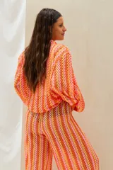 Conjunto de dos piezas tejido a crochet con diseño de ondas en tonos naranja, rosado y amarillo, compuesto por una camisa de manga larga y un pantalón largo de corte recto.