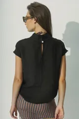 Blusa de lino color negro, con cuello alto y mangas cortas con detalle de costura decorativa en los hombros. Presenta un diseño minimalista de silueta recta y tejido liviano.