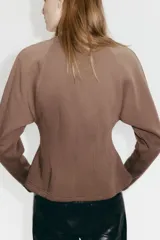 Buzo de felpa con interior cepillado, cuello redondo acanalado y mangas largas raglán. Presenta costuras moldeadoras en la cintura que crean una silueta entallada con efecto peplum.