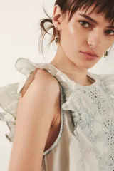 Camisa sin mangas color blanco roto, con volados en los hombros y bordado estilo calado en el frente con motivos florales en hilo celeste.