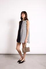 Vestido corto sin mangas con escote recto, confeccionado con paneles combinados: un lado negro liso y el otro blanco con estampado de lunares negros. Posee bolsillos ocultos laterales.