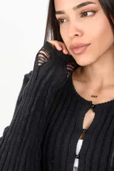 Cardigan corto de tejido de punto acanalado en color negro, con mangas largas y detalles desgastados o rotos en el frente y puños. Cierre frontal con pequeños botones redondos.