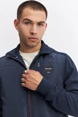 Campera de estilo deportivo con cierre frontal, confeccionada en una combinación de nylon y algodón. Presenta un diseño con paneles texturizados en las mangas, cuello alto y un parche decorativo con coordenadas en el pecho.