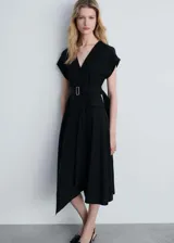 Vestido midi de corte evasé en color negro, con cuello en pico y diseño sin mangas. Presenta un cinturón ajustable con hebilla metálica en la cintura, dos bolsillos con solapa en la parte frontal y un bajo asimétrico.