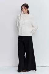 Sweater de punto color blanco off-white, con cuello redondo y diseño texturizado con trenzas y pompones en el frente.