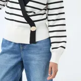 Sweater de punto con diseño cruzado tipo cárdigan, de manga larga y cuello en V. Presenta un estampado de rayas horizontales negras sobre fondo blanco, con bordes negros y un botón dorado decorativo en el frente.