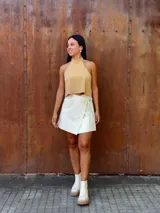 Falda corta tipo wrap de cuero color crudo, con diseño cruzado y ajuste mediante tiritas laterales.