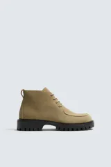 Bota de caña baja con cordones, confeccionada en piel con acabado de serraje. Presenta horma redonda, detalle de costura en el empeine y suela track con volumen.